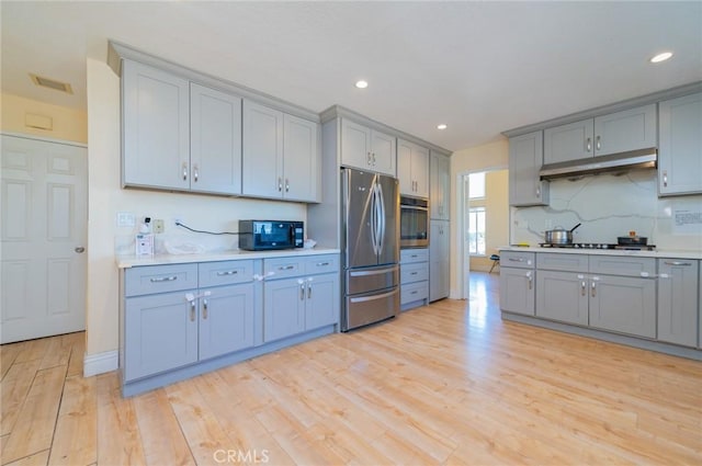 kitchen with under cabinet range hood, light countertops, appliances with stainless steel finishes, and gray cabinets