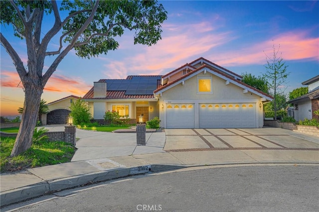 view of front of house featuring a tiled roof, solar panels, a garage, stucco siding, and concrete driveway