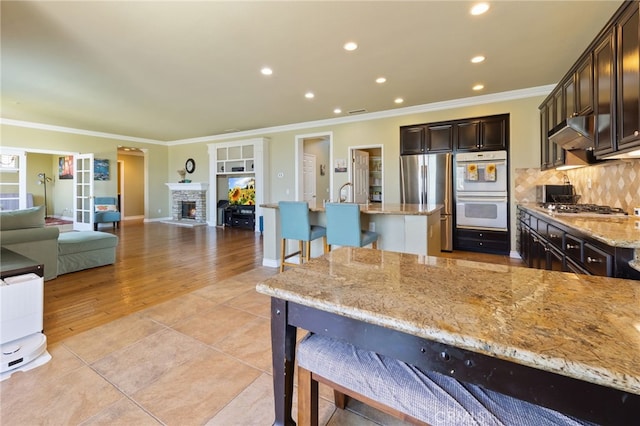 16673 Carob Ave, Chino Hills, CA 91709 - kitchen featuring stainless steel appliances, a breakfast bar area, dark brown cabinets, ornamental molding, and light stone countertops