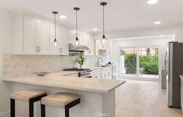 kitchen featuring under cabinet range hood, light stone counters, a sink, white cabinetry, and appliances with stainless steel finishes