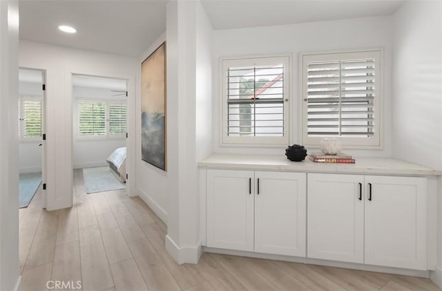 hall featuring light wood-style flooring, baseboards, and recessed lighting