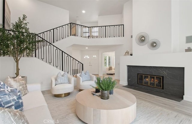 living area with baseboards, a high end fireplace, a towering ceiling, wood finished floors, and stairway
