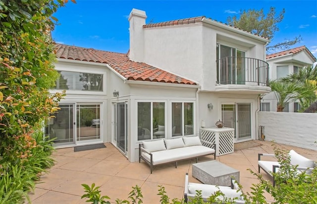 back of property featuring a tiled roof, a patio area, a chimney, and a balcony