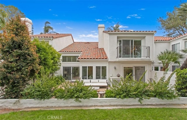 rear view of property with a chimney, a balcony, stucco siding, and a tiled roof