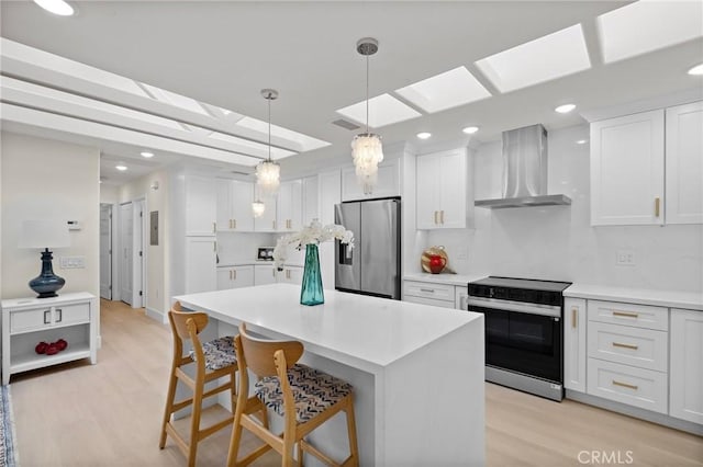 kitchen with white cabinetry, stainless steel fridge, wall chimney exhaust hood, light wood-style floors, and electric range