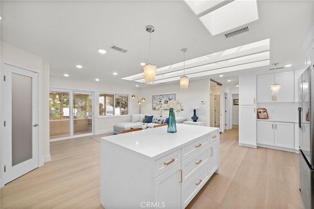 663 Via Los Altos Unit Q, Laguna Woods, CA 92637 - kitchen featuring open floor plan, white cabinets, light wood finished floors, a center island, and hanging light fixtures
