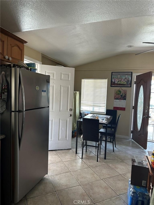 kitchen featuring freestanding refrigerator, lofted ceiling, a textured ceiling, light tile patterned floors, and brown cabinets