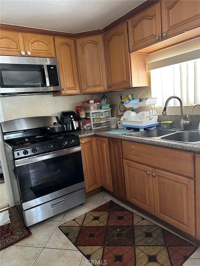 kitchen with a sink, stainless steel appliances, light tile patterned floors, and brown cabinets