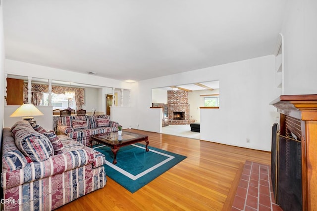 living room featuring a brick fireplace, visible vents, and wood finished floors