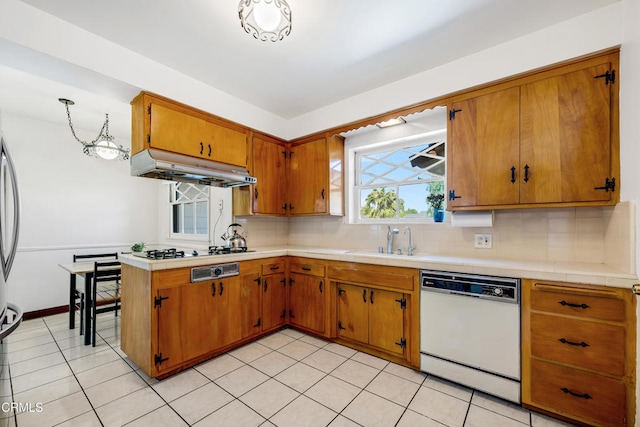 kitchen with a sink, brown cabinetry, tasteful backsplash, under cabinet range hood, and white dishwasher