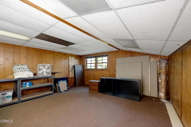 interior space with wooden walls, carpet floors, and a drop ceiling