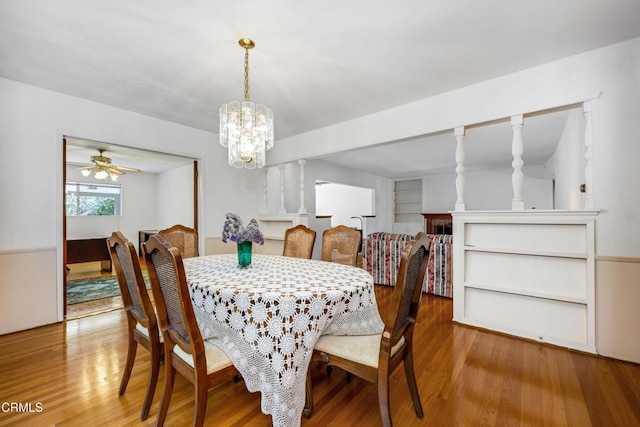 dining area with ceiling fan with notable chandelier, built in features, and wood finished floors