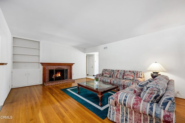 living area with wood finished floors, visible vents, a fireplace, and built in features