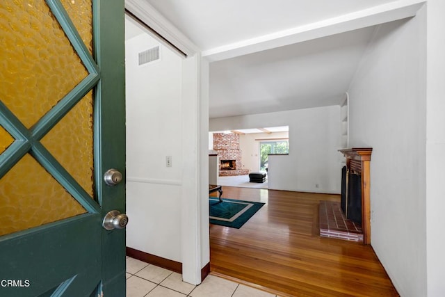 tiled entryway with visible vents and a brick fireplace
