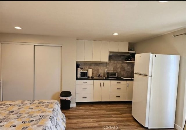 kitchen with freestanding refrigerator, recessed lighting, under cabinet range hood, dark wood-style flooring, and tasteful backsplash
