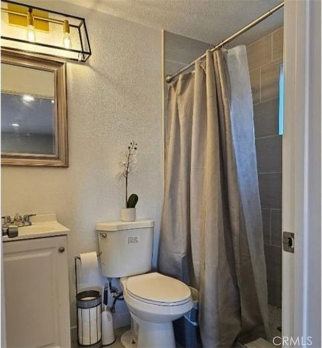 full bath with toilet, tiled shower, vanity, and a textured wall