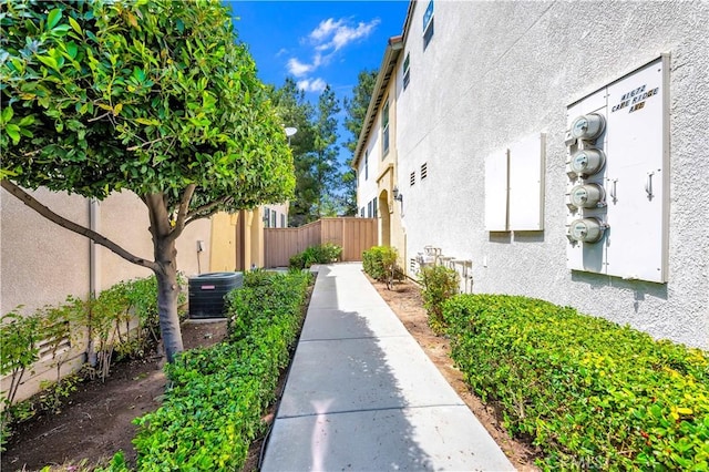 view of side of property with central AC, stucco siding, and fence