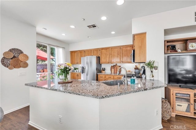 kitchen featuring a sink, a peninsula, stainless steel appliances, visible vents, and light stone countertops