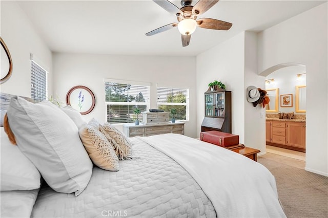 bedroom featuring lofted ceiling, ensuite bathroom, ceiling fan, arched walkways, and light colored carpet