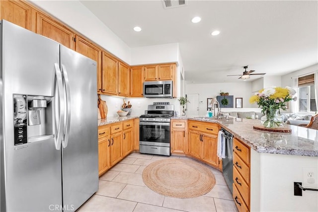 kitchen featuring a sink, a peninsula, stainless steel appliances, ceiling fan, and light stone countertops