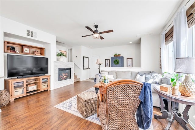 living room featuring ceiling fan, a glass covered fireplace, visible vents, and wood finished floors