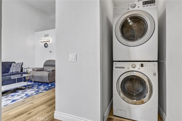 laundry area with laundry area, stacked washer and dryer, baseboards, and wood finished floors