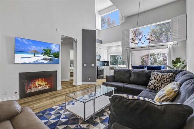 living area featuring light wood finished floors, a warm lit fireplace, baseboards, and a high ceiling
