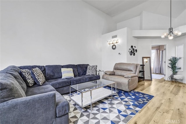 living room featuring an inviting chandelier, lofted ceiling, visible vents, and light wood-style floors