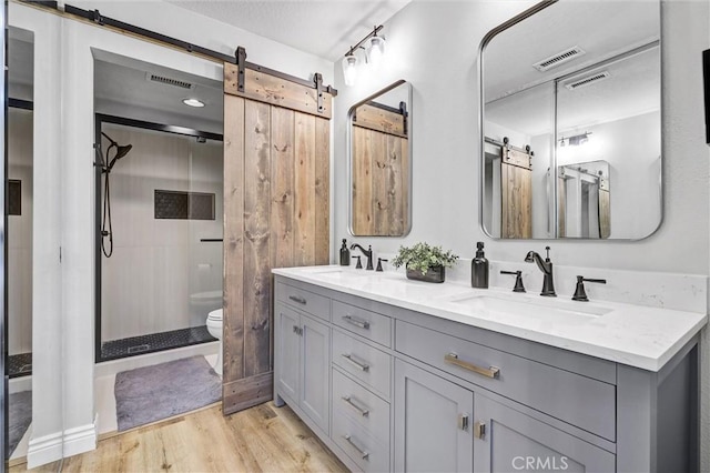 bathroom with toilet, a stall shower, a sink, and wood finished floors