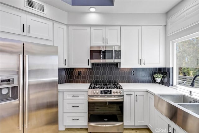kitchen with a sink, stainless steel appliances, visible vents, white cabinetry, and light countertops