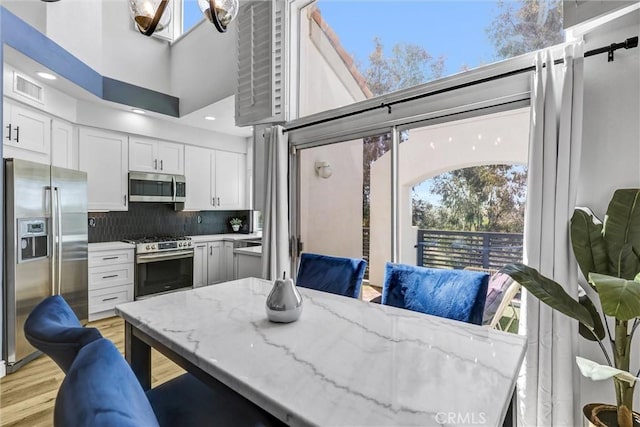 kitchen featuring stainless steel appliances, tasteful backsplash, light stone counters, visible vents, and white cabinets
