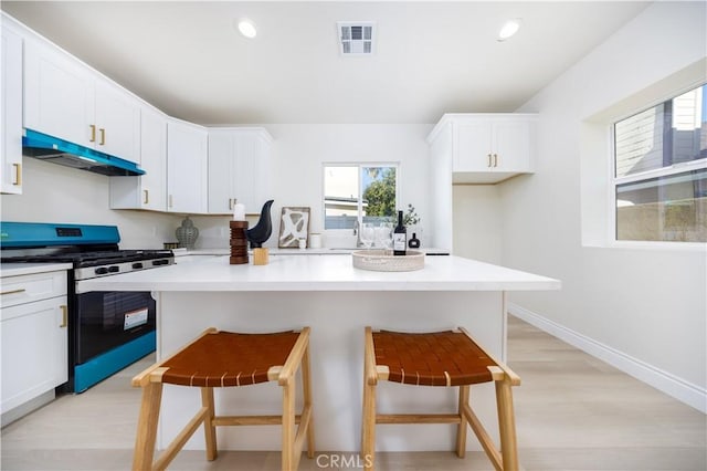 737 Lewis St, Pomona, CA 91768 - kitchen featuring under cabinet range hood, visible vents, white cabinetry, a kitchen breakfast bar, and stainless steel range with gas cooktop