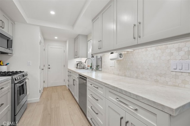 kitchen with light wood-style flooring, recessed lighting, a sink, backsplash, and appliances with stainless steel finishes