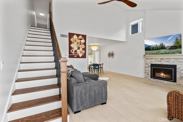 staircase with wood finished floors, a ceiling fan, a fireplace, visible vents, and a towering ceiling