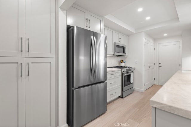 kitchen featuring recessed lighting, light wood finished floors, a raised ceiling, stainless steel appliances, and tasteful backsplash