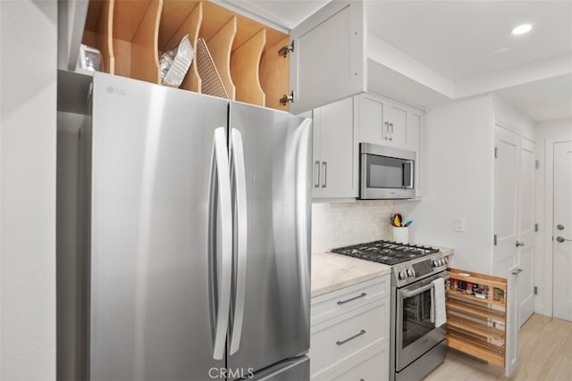 kitchen with white cabinetry, light wood-type flooring, tasteful backsplash, appliances with stainless steel finishes, and light stone counters