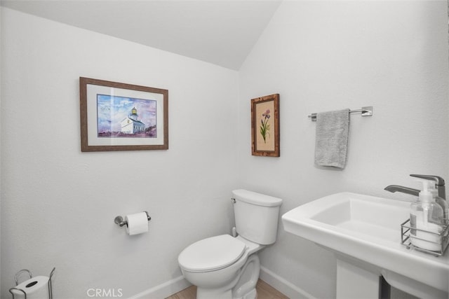 bathroom with a sink, lofted ceiling, toilet, wood finished floors, and baseboards