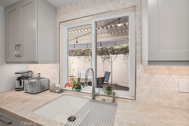 kitchen featuring gray cabinetry, a toaster, tasteful backsplash, and a sink