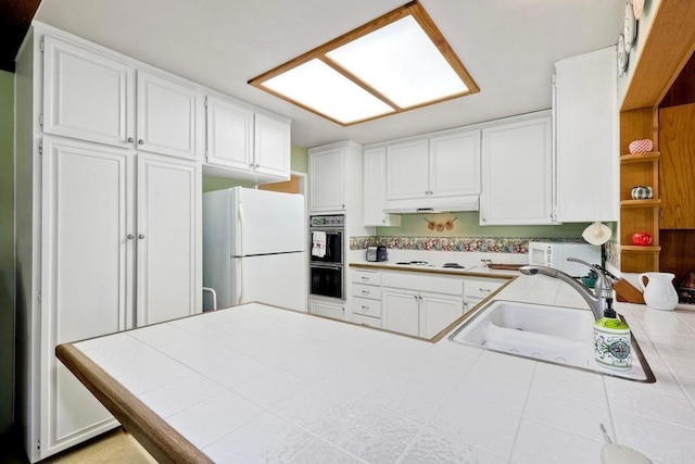 kitchen with tile counters, white appliances, a peninsula, and a sink
