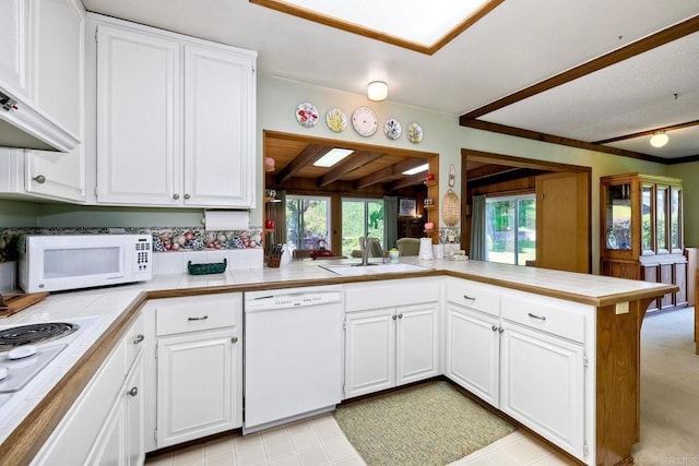 kitchen with white appliances, a sink, white cabinetry, a peninsula, and tile counters