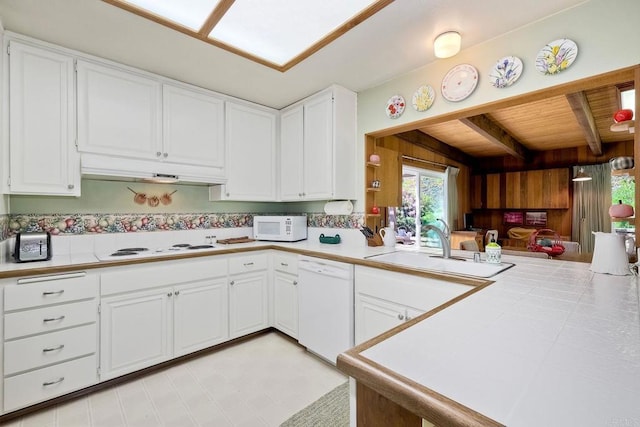 kitchen with under cabinet range hood, white appliances, a peninsula, tile counters, and beam ceiling