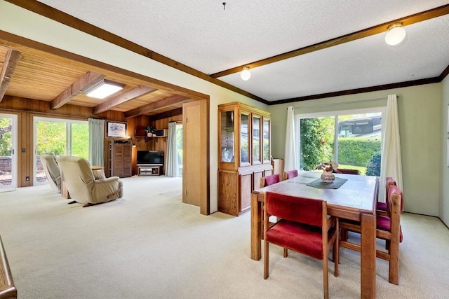 dining room with beamed ceiling, light carpet, wooden walls, and plenty of natural light