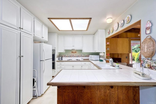 kitchen featuring a sink, a peninsula, white appliances, white cabinetry, and tile counters