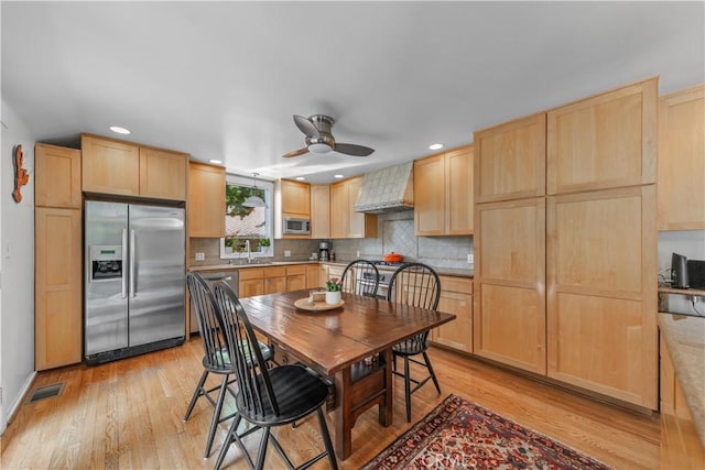 kitchen with a sink, a ceiling fan, light brown cabinets, custom range hood, and appliances with stainless steel finishes
