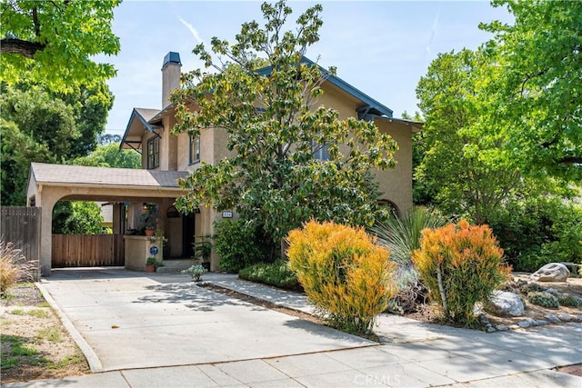 view of front facade featuring a chimney, driveway, fence, stucco siding, and a carport