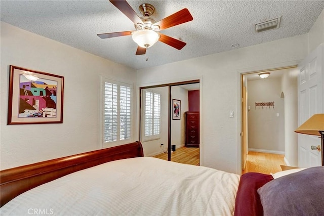 bedroom featuring a closet, a textured ceiling, ceiling fan, visible vents, and light wood-style floors