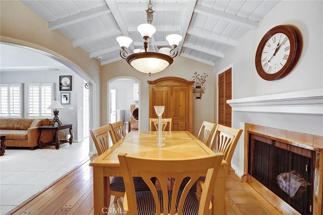 dining area with a fireplace, washer / clothes dryer, lofted ceiling with beams, and arched walkways