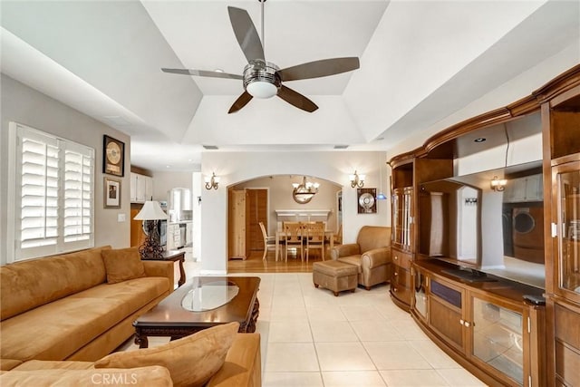 living room featuring light tile patterned floors, ceiling fan with notable chandelier, visible vents, a raised ceiling, and arched walkways