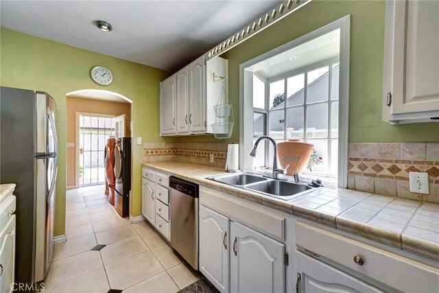 kitchen featuring light tile patterned floors, a sink, decorative backsplash, arched walkways, and stainless steel appliances