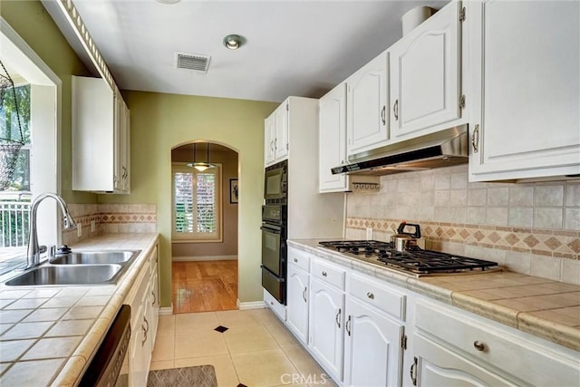 kitchen featuring a sink, tile counters, visible vents, under cabinet range hood, and stainless steel gas cooktop